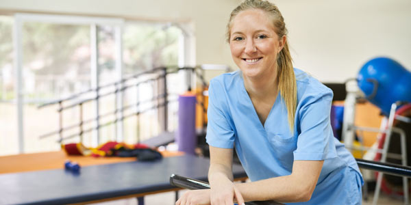 Image of smiling female physio with therapy equipment in the background. Representing the physios, OTs and healthcare professionals we work with.