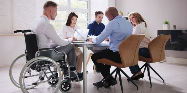 Image of of 5 people around a meeting table, one is in a wheelchair. Representing our work with Case Managers and their clients.