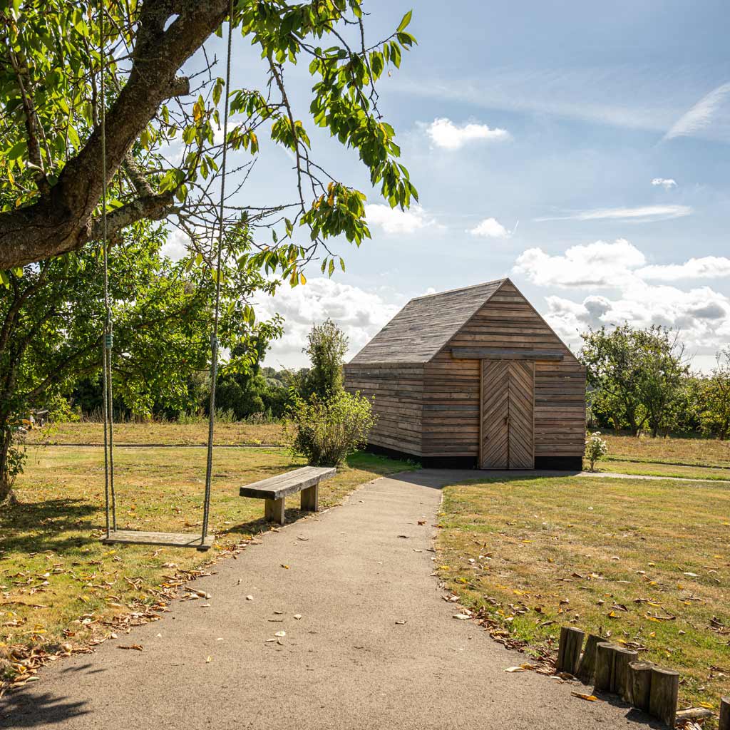 Accessible family garden with wheel-chair friendly paths and a stylish modern wood cabin. A swing hangs from a nearby tree.