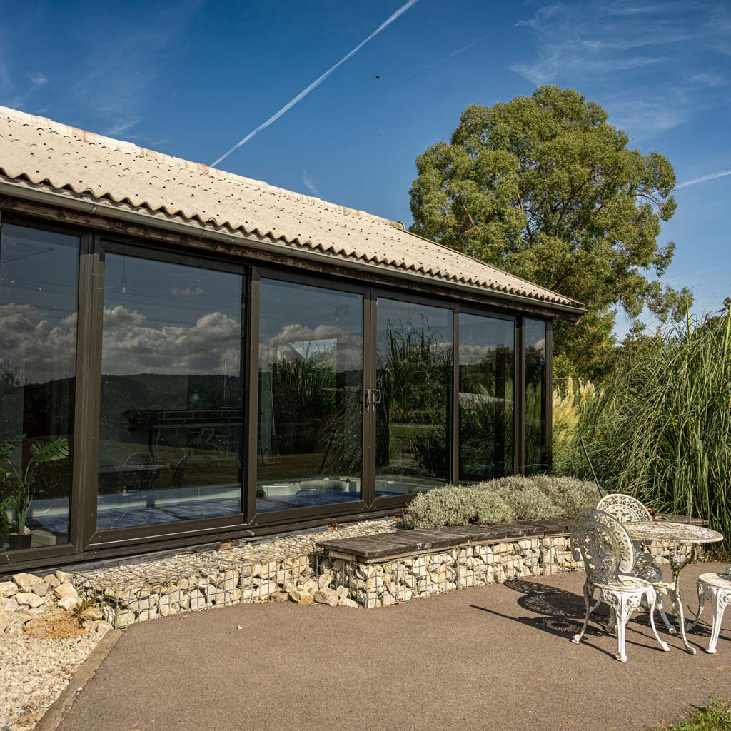 Modern glass-fronted outdoor hydrotherapy annexe set in an accessible garden.