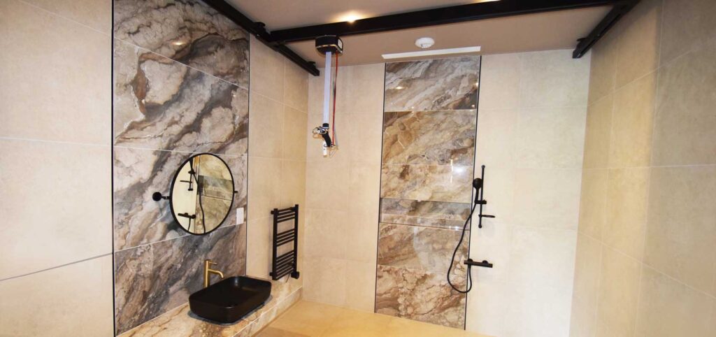 Photo of high-end disability adapted wetroom with marble walls and custom black ceiling track.