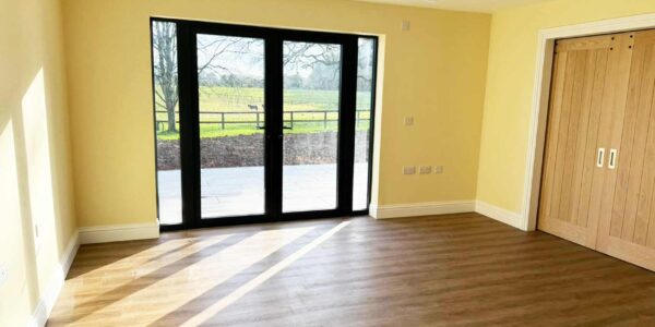 Bright and airy bedroom with en-suite wheelchair accessible wet room. Double doors with level access overlook a patio area and sweeping countryside views.