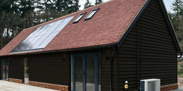 Back view of the accessible annexe with solar panels on the roof and a heat source pump outside. Traditional tiled roof and black wood cladding blend the building with its historic setting.