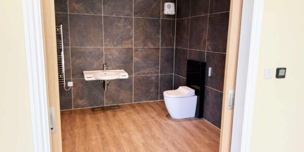 Modern accessible wetroom with natural stone tile walls and chrome fittings. Features include a Geberit Aquaclean bidet toilet and roll under sink.