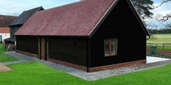 Accessible annexe in Canterbury seen from the front. A single-storey wheelchair adapted annexe with solar panels and heat source pump outside. Black wood cladding blends the building with the heritage landscape.