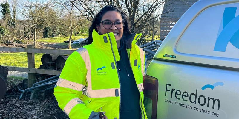 Photo of Sam Mohabir in a high-vis jacket standing next to a an with the Freedom living Solution logo